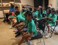 Children in green shirts sitting attentively.